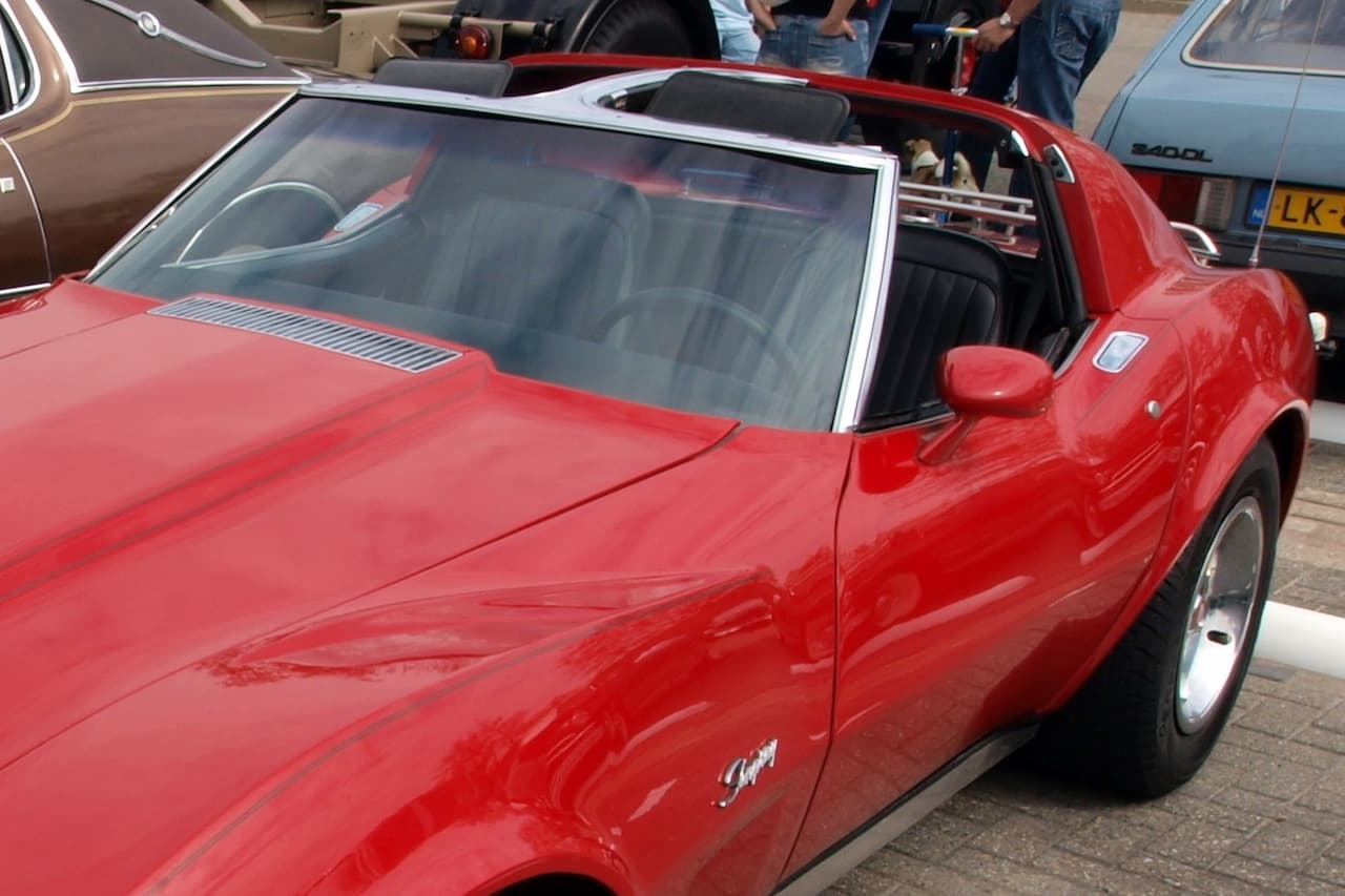 Red classic sports car with removable T-top roof panels, showing tinted glass and chrome trim at car show