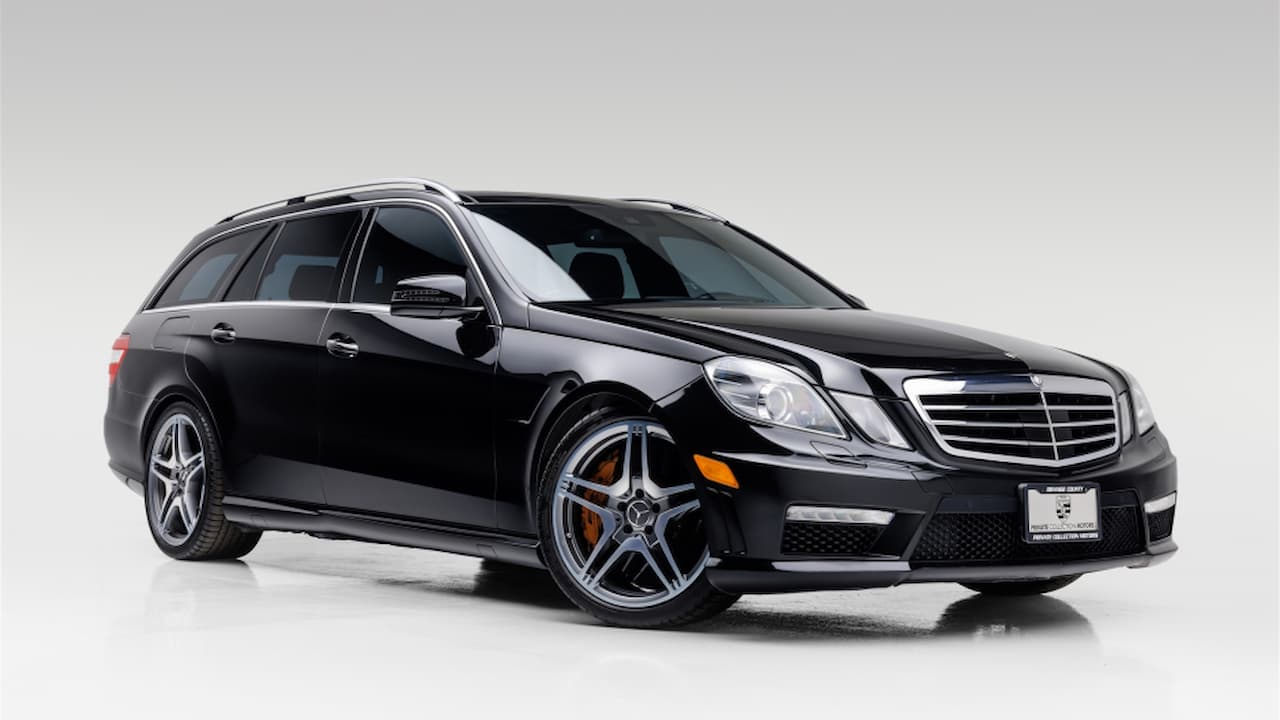 Black Mercedes-Benz E63 AMG wagon with silver five-spoke wheels and orange brake calipers on white studio background