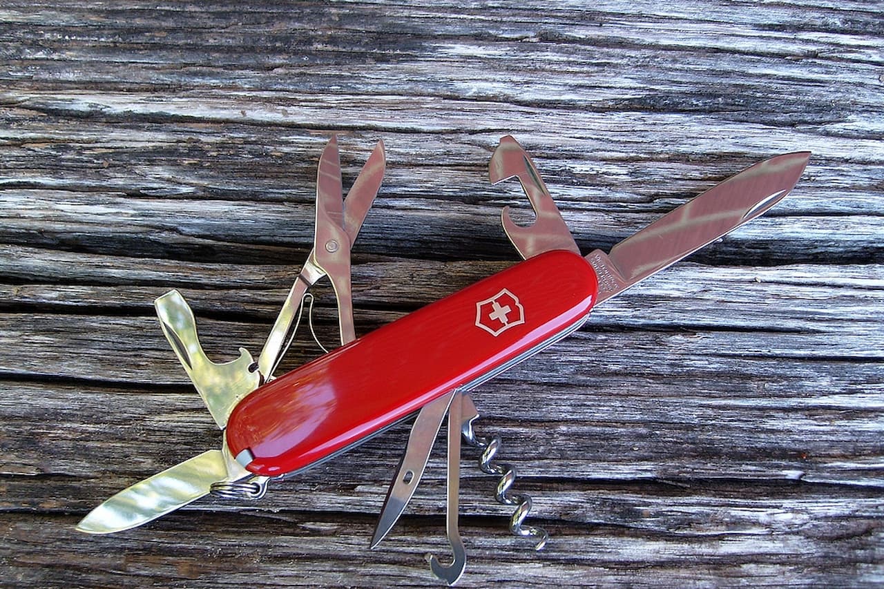 Red Swiss Army knife with multiple tools extended including scissors, blade, and corkscrew on weathered wooden surface