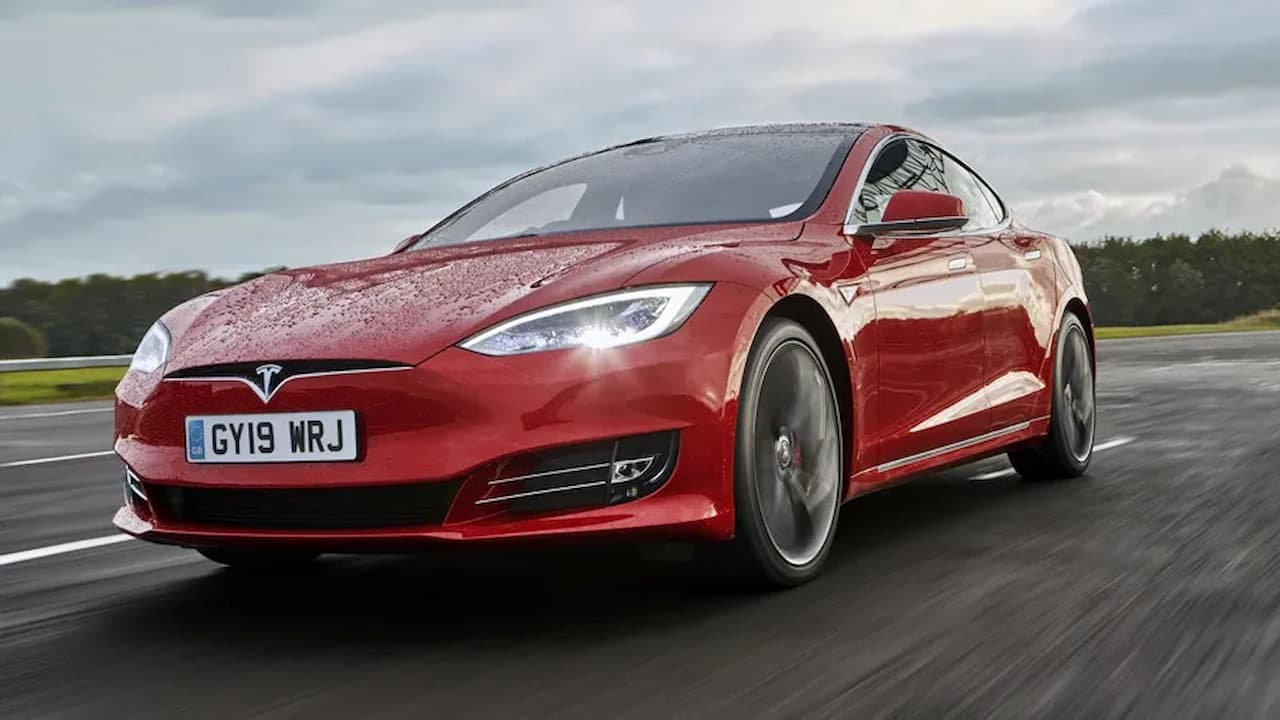 Red Tesla Model S Performance driving on wet road with motion blur, showing sleek electric sedan design