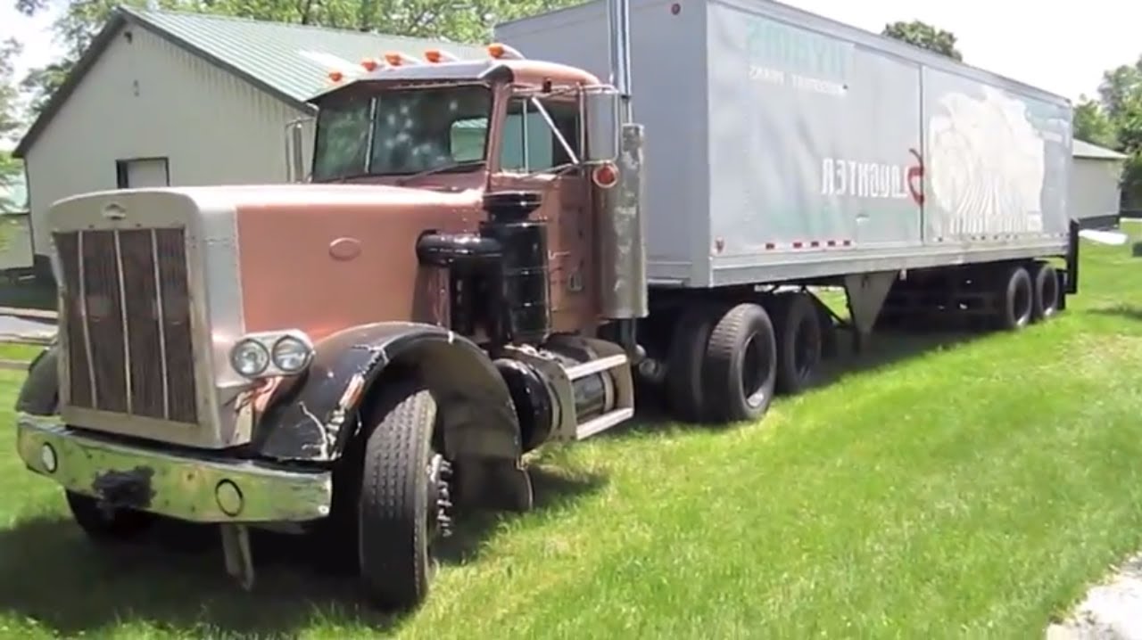 Large semi-truck with white trailer parked on green grass near residential buildings and trees