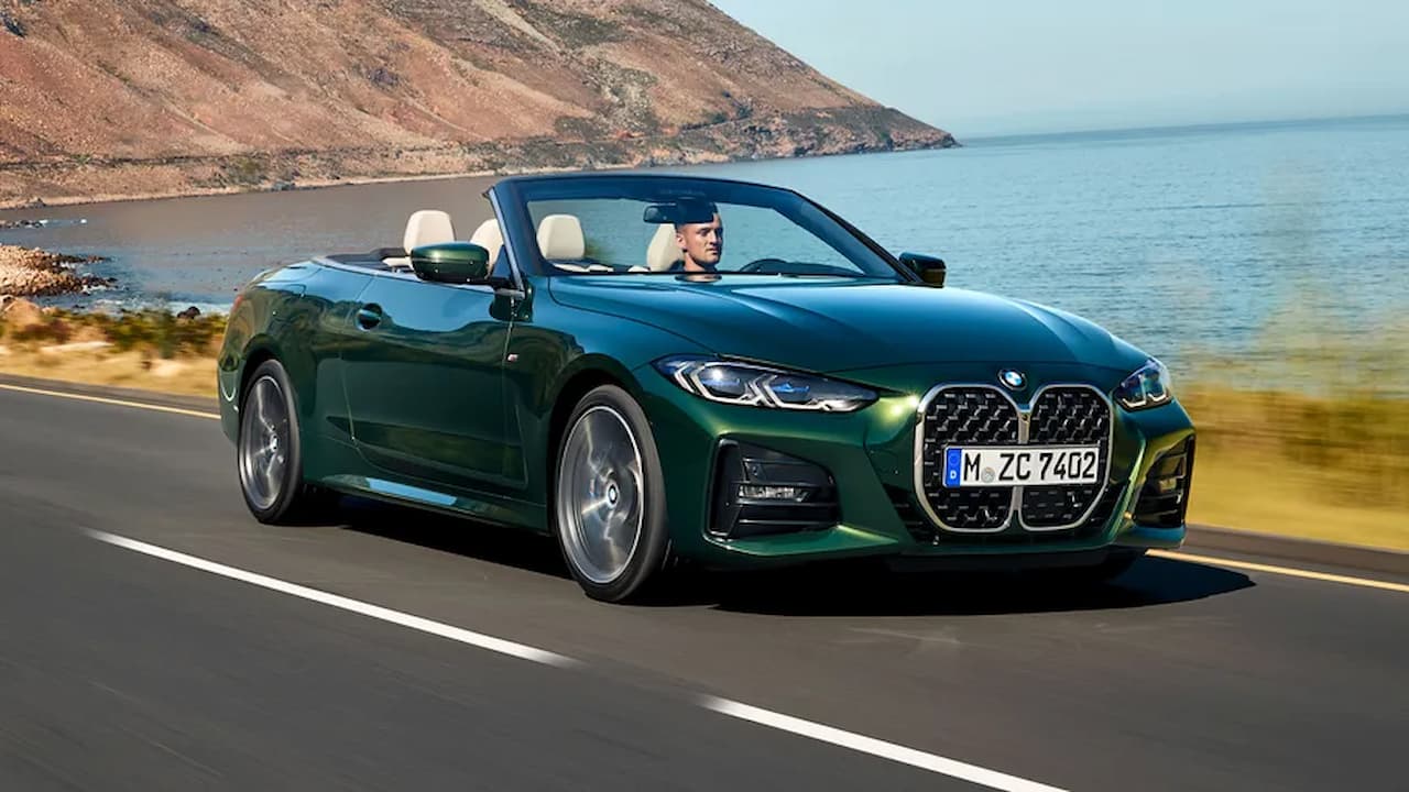 Green BMW 4 Series convertible driving on coastal road with driver, ocean and hills visible in background