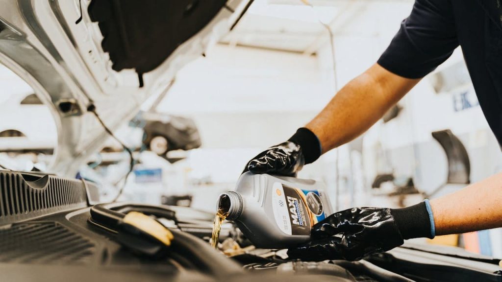 Mechanic wearing black gloves pouring motor oil from container into car engine during oil change service