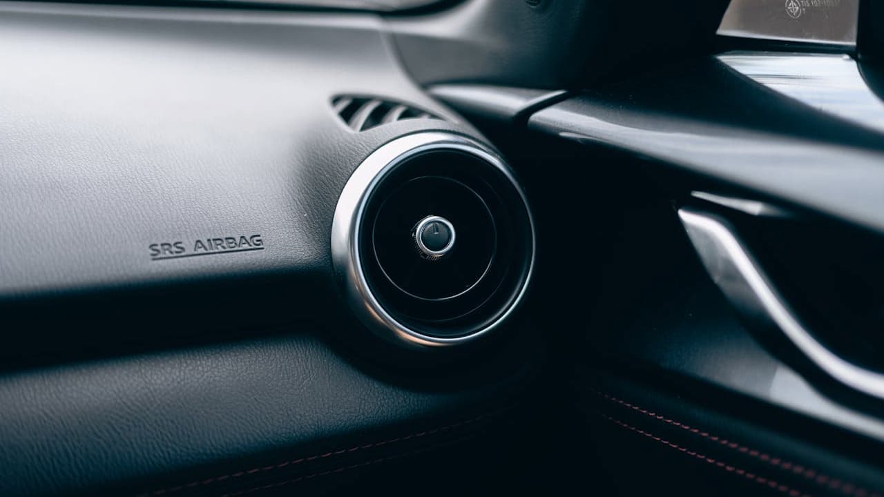 Close-up of modern car dashboard showing circular air vent with chrome trim and "SRS AIRBAG" safety marking