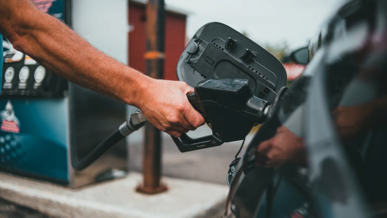 Person's hand holding black gas pump nozzle inserting it into car's fuel tank at service station