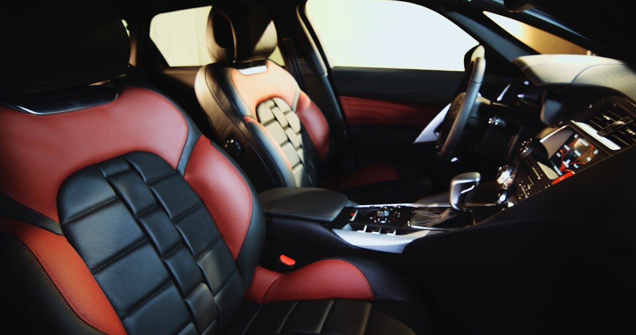 Car interior with red and black quilted leather seat covers, dashboard, steering wheel, and center console visible