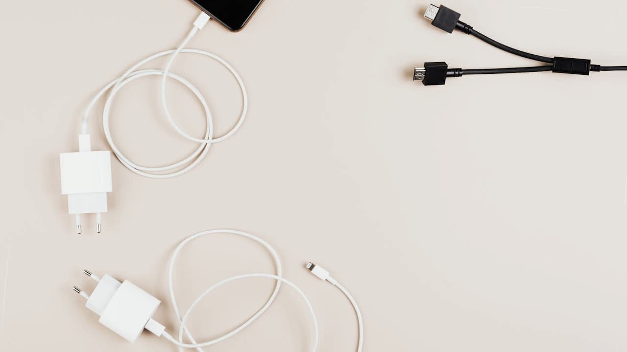 White and black phone charging cables with wall adapters and USB connectors on light beige surface