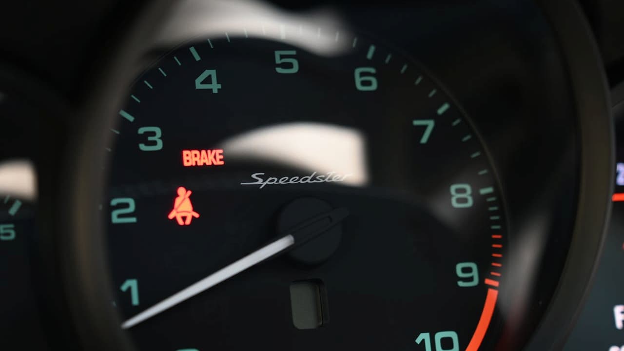 Car dashboard showing illuminated red "BRAKE" warning light and red brake system icon on speedometer displaying "Speedster" brand name