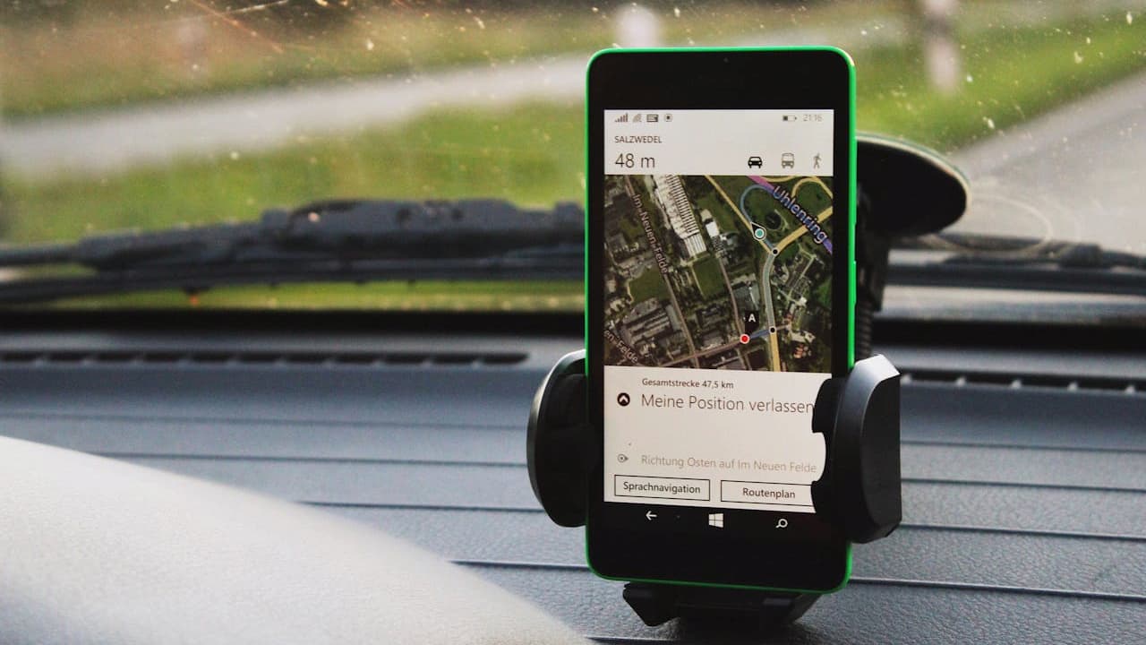 Smartphone in car dashboard mount displaying GPS navigation map with German text, showing route directions and current location