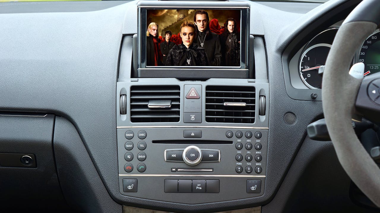 Car dashboard infotainment system with built-in screen displaying movie content, surrounded by control buttons, air vents, and steering wheel