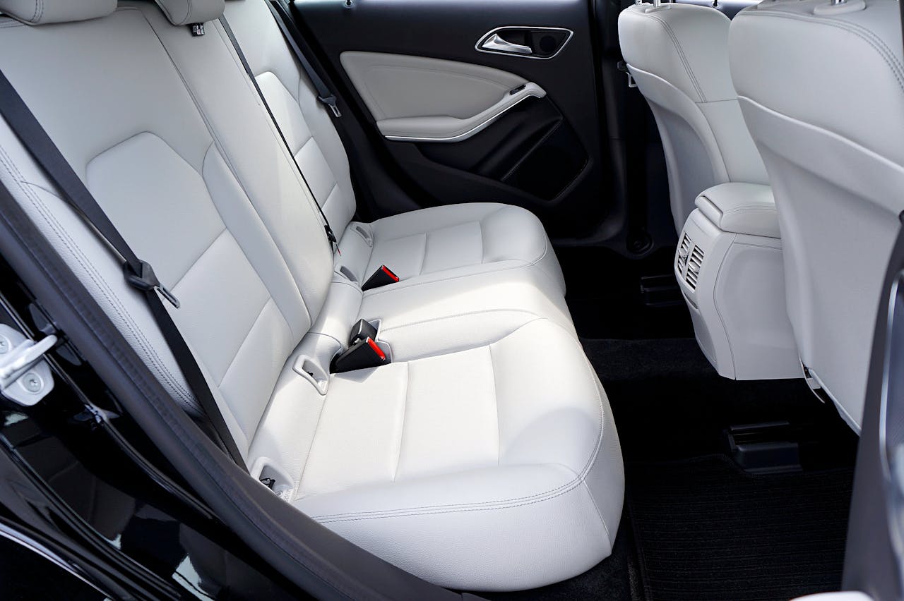 Clean white leather car interior showing rear seats with seatbelts, door panels, and black carpet flooring