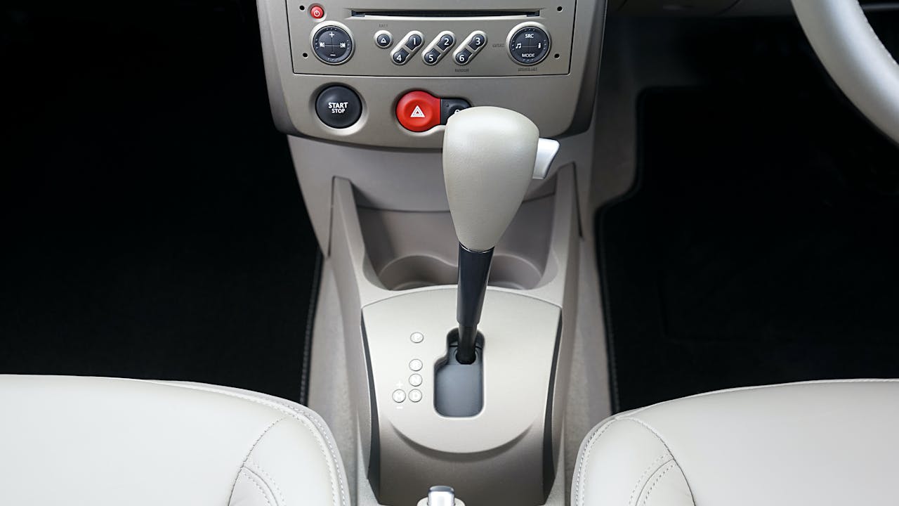 Car center console showing automatic window controls, climate controls, start/stop button, hazard lights, and white leather seats