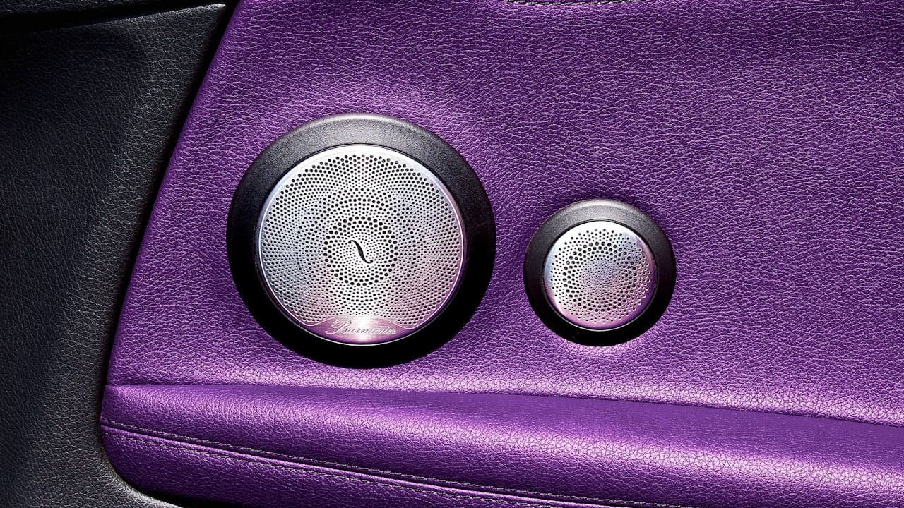 Two premium car speakers with perforated metal grilles and chrome rings mounted in purple leather automotive interior panel