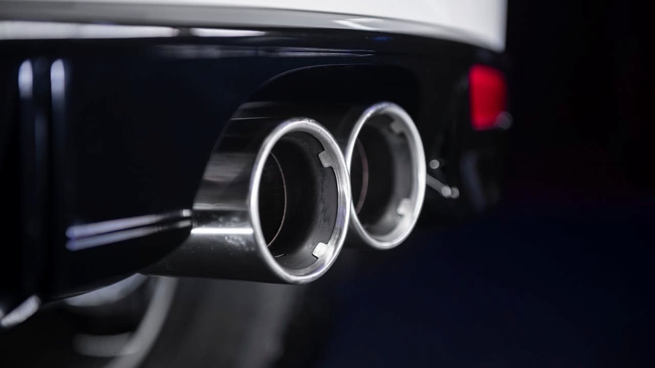 Close-up of dual chrome exhaust pipes on black car rear bumper, showing polished circular tailpipes and performance exhaust system