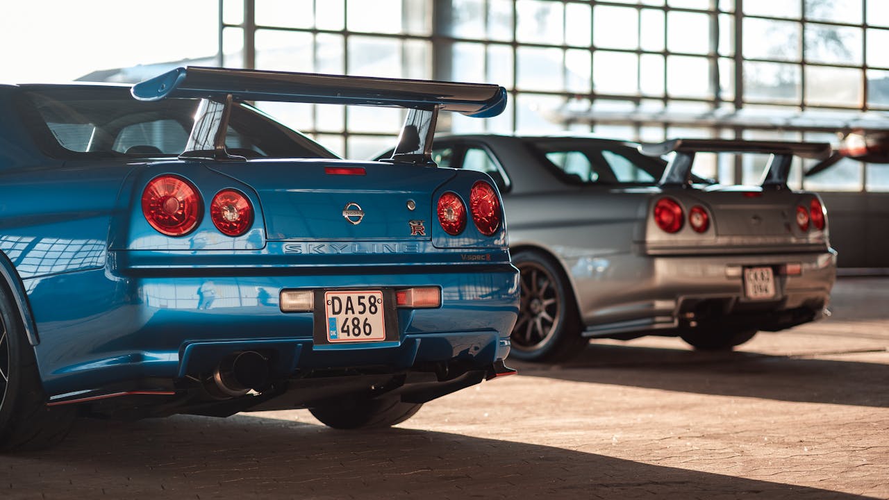 Blue Nissan Skyline GT-R with large rear spoiler parked in garage alongside other Japanese sports cars with spoilers