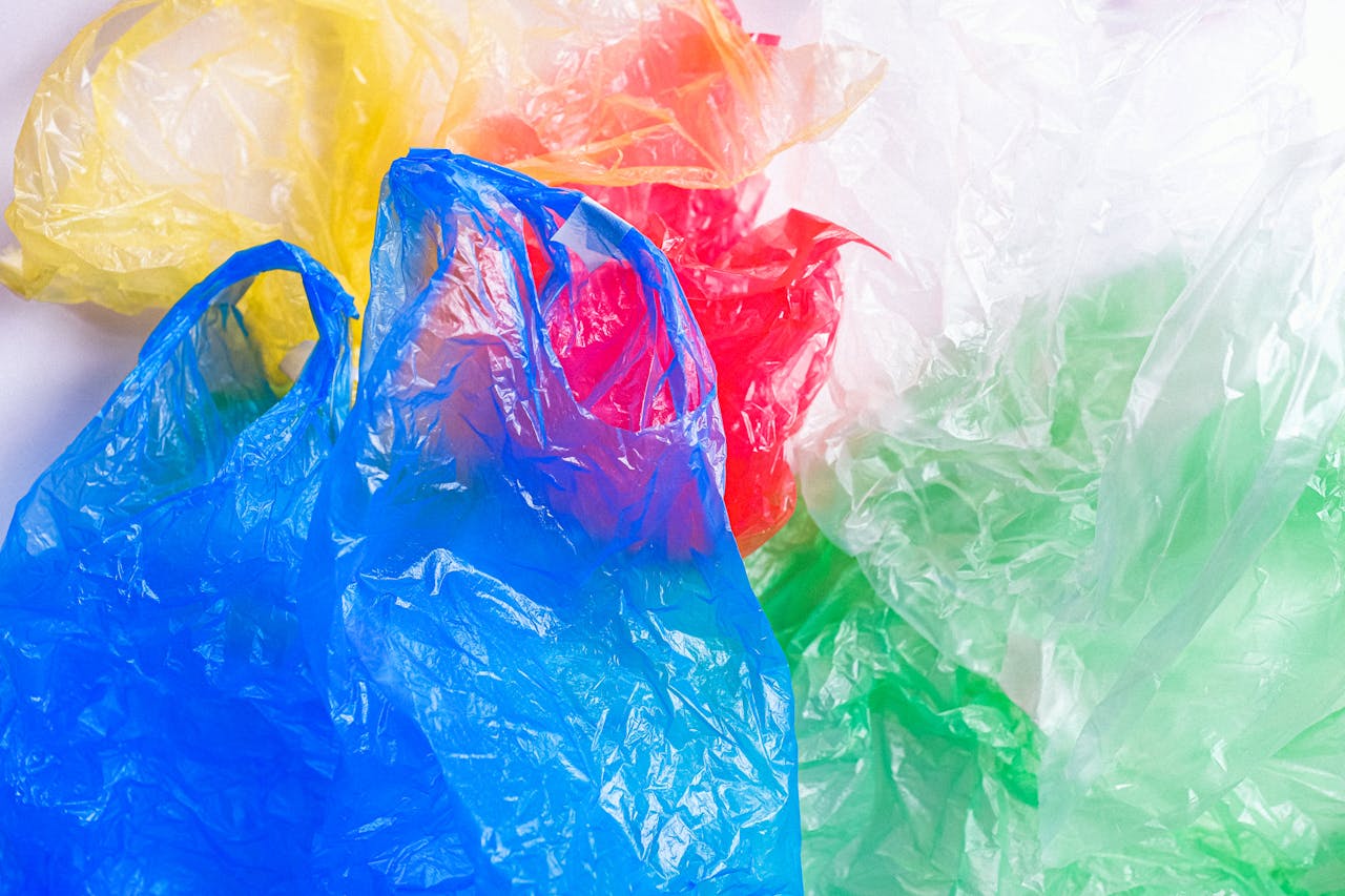 Colorful crumpled plastic waste bags in blue, yellow, red, clear, and green scattered on white background surface