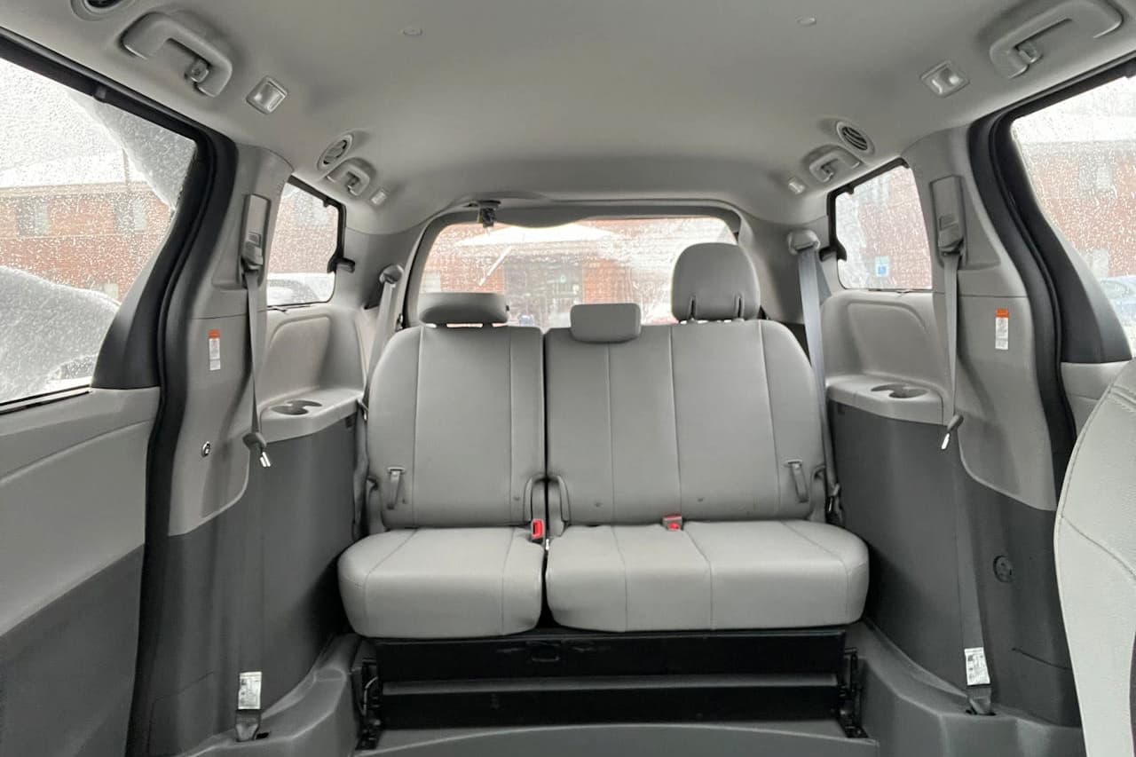 Toyota Sienna minivan interior showing gray leather third-row bench seat with cup holders, windows, and light gray cabin styling