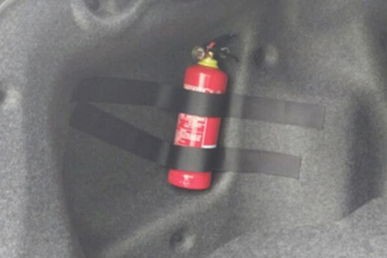A red and black fire extinguisher with yellow safety pin is secured in gray vehicle trunk compartment