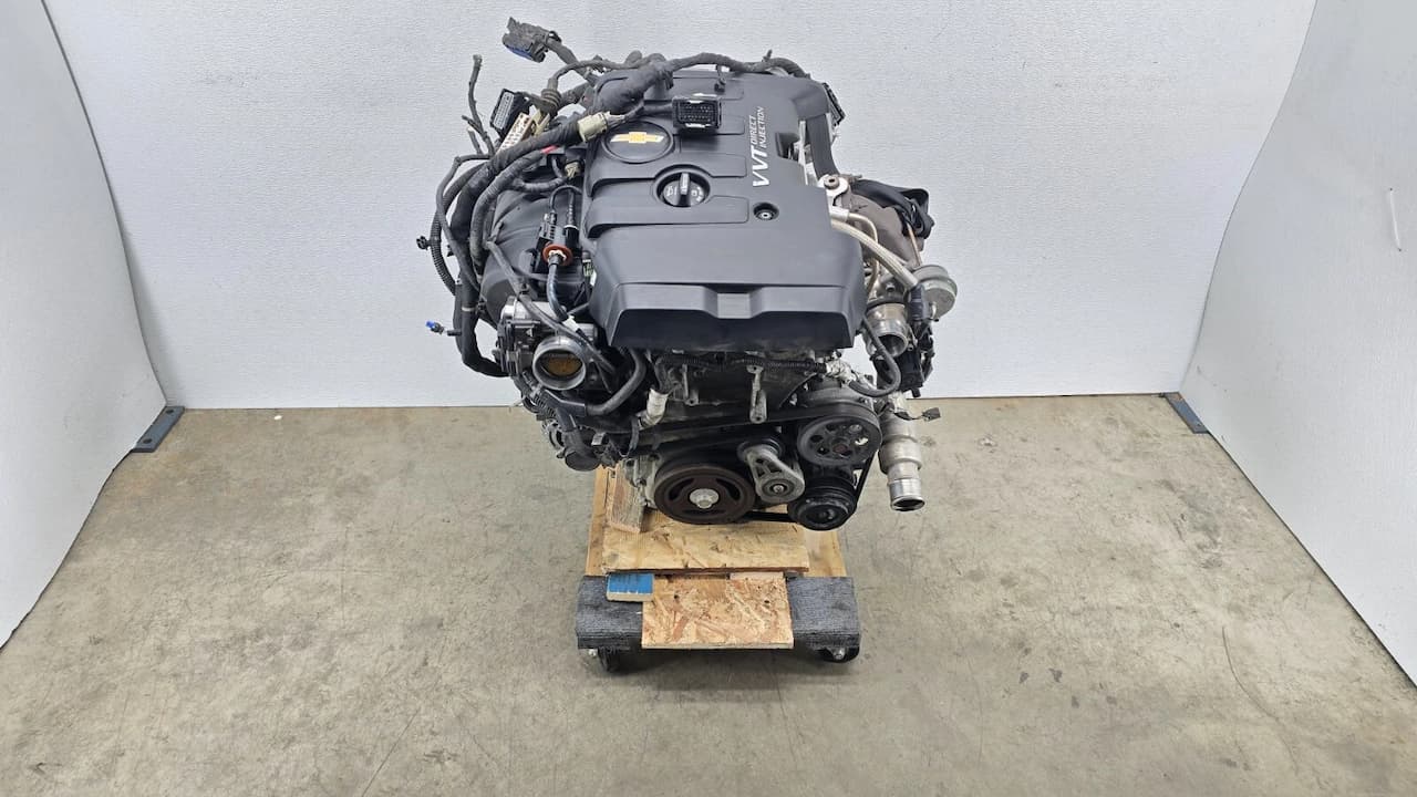 Chevrolet 2.0L Turbo engine assembly on wooden pallet with black plastic cover, extensive wiring harnesses, and accessory components