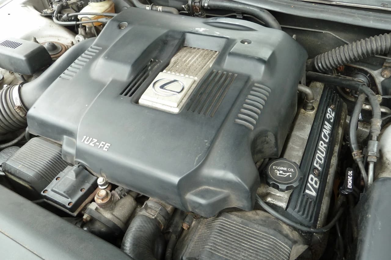 Lexus LS400 1UZ-FE V8 engine bay showing gray plastic engine cover, Lexus badge, oil filler cap, and surrounding components