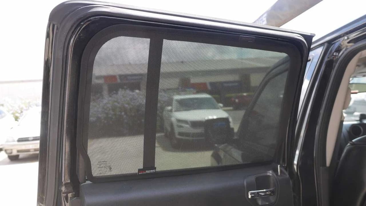 A mesh sunshade installed on rear car window blocks sunlight while allowing visibility of parking lot outside