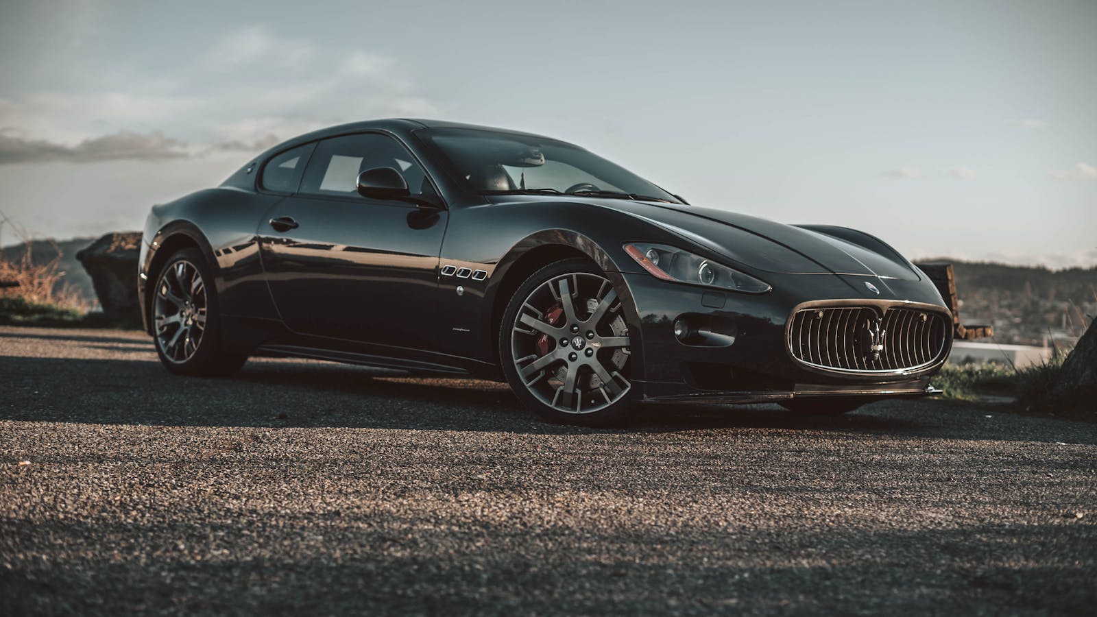 Luxurious black Maserati captured on an open road at sunset, highlighting its elegant design.