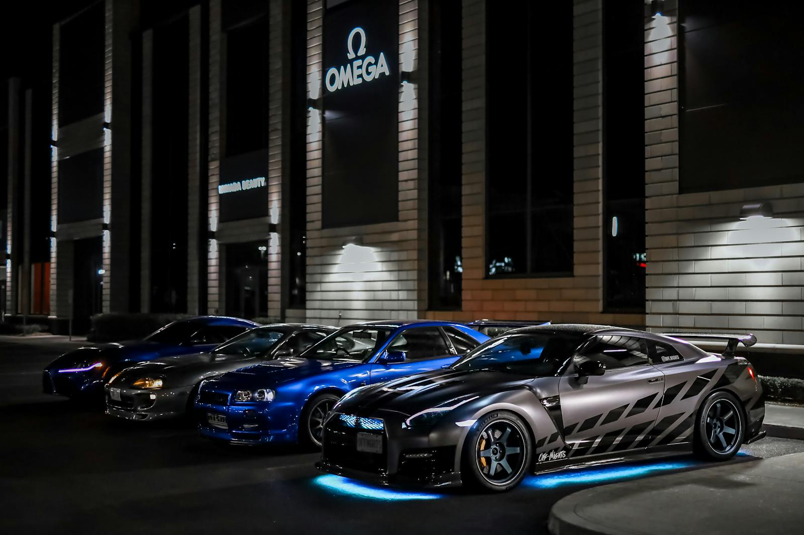 A lineup of modified Nissan sports cars parked at night in an illuminated urban setting.