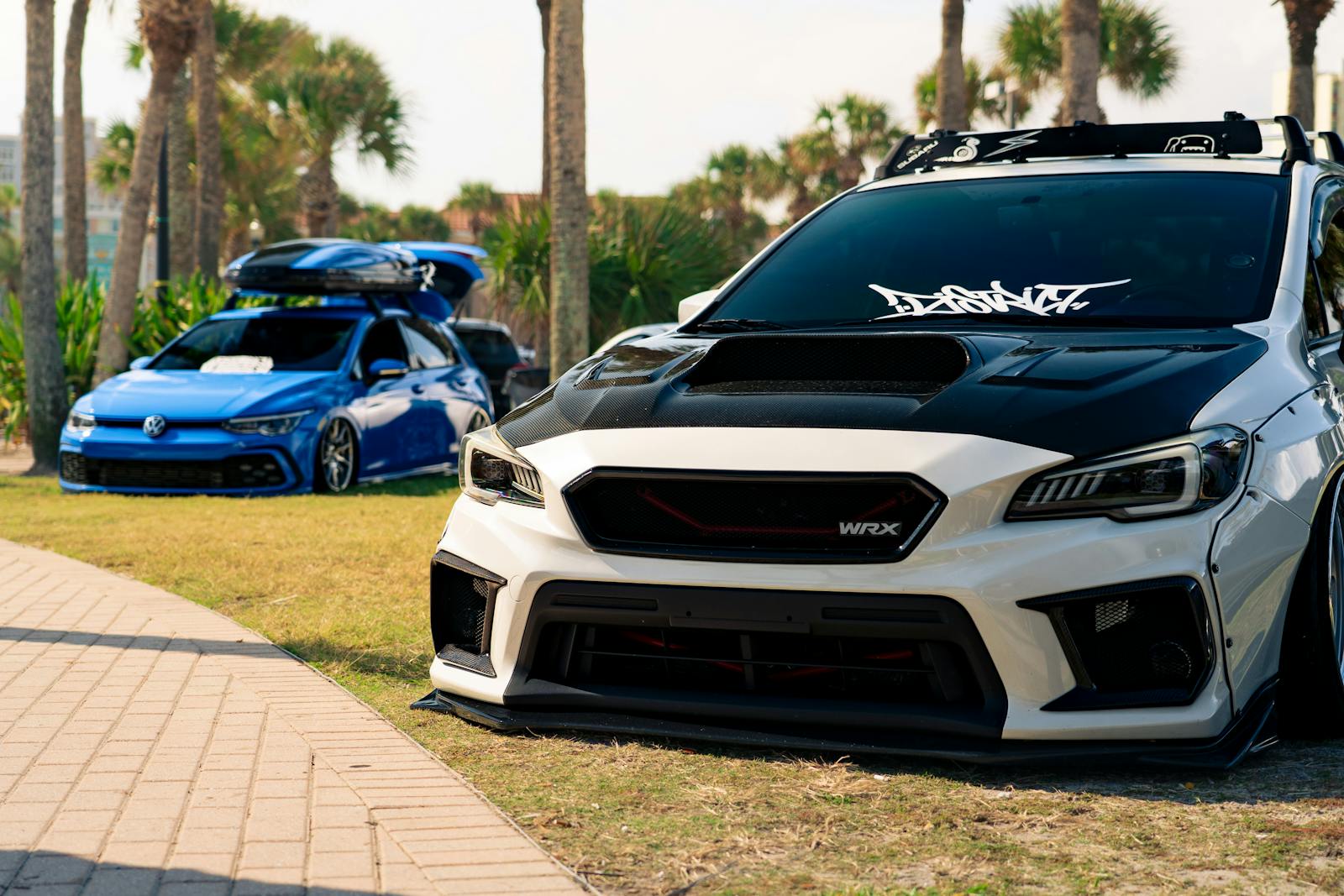 Showcasing heavily modified cars in an outdoor setting under palm trees.