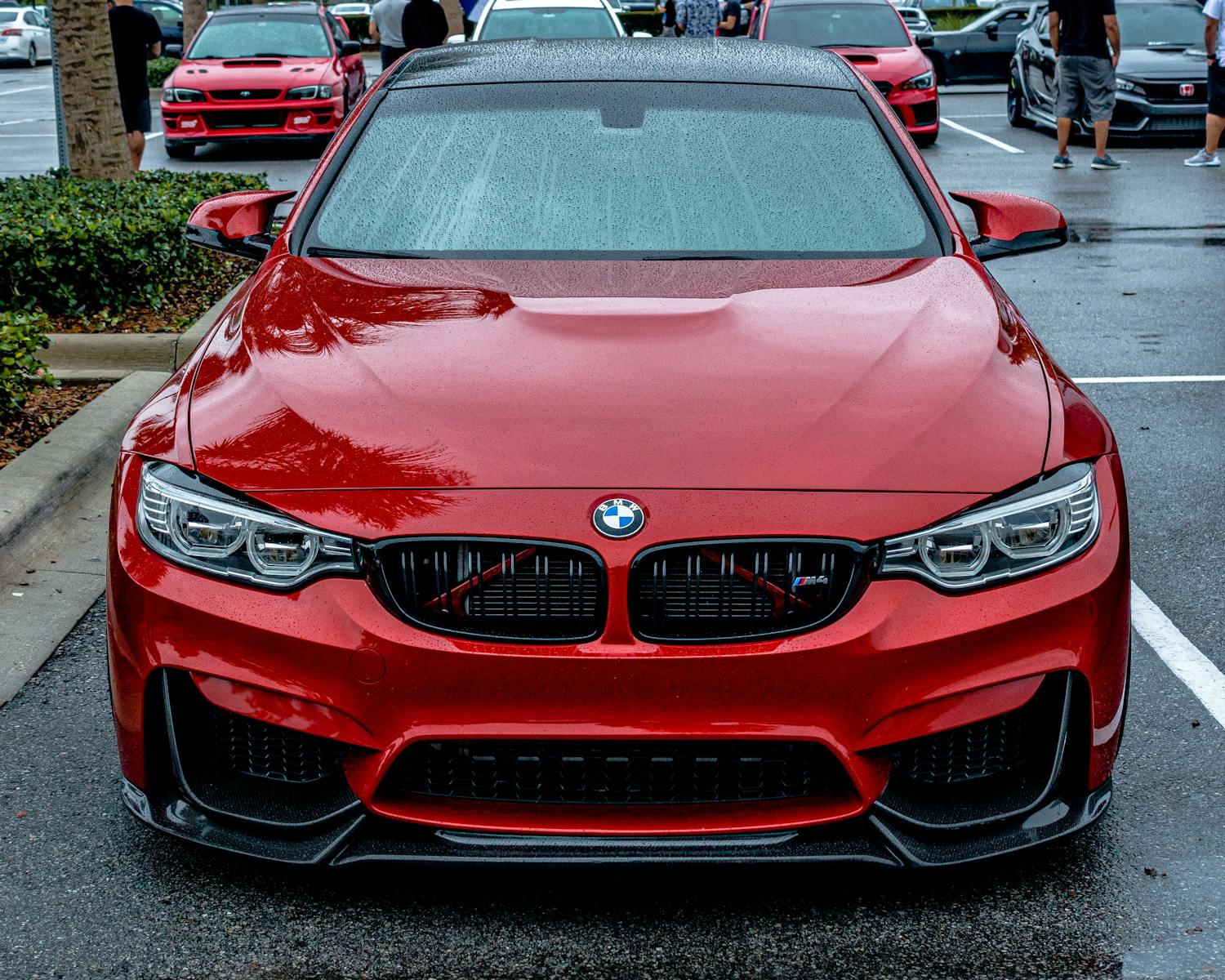 Front view of a sleek red BMW car with rain droplets in an Orlando parking lot.