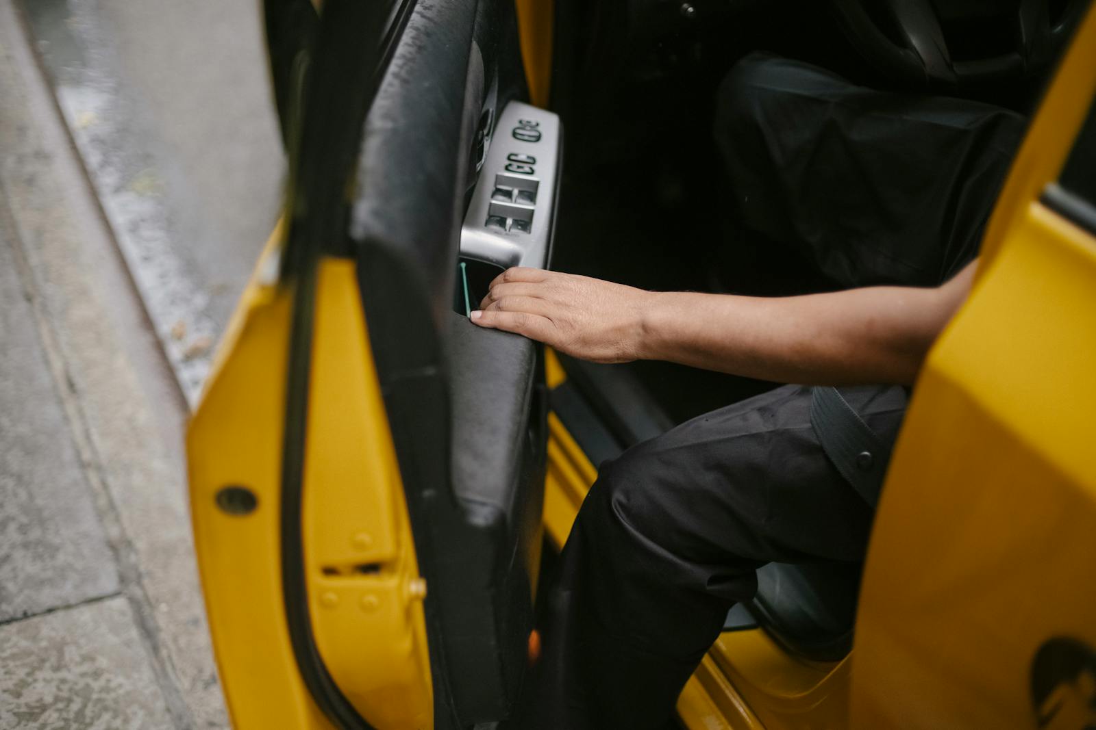 Close-up of a person opening a yellow taxi door on a city street.