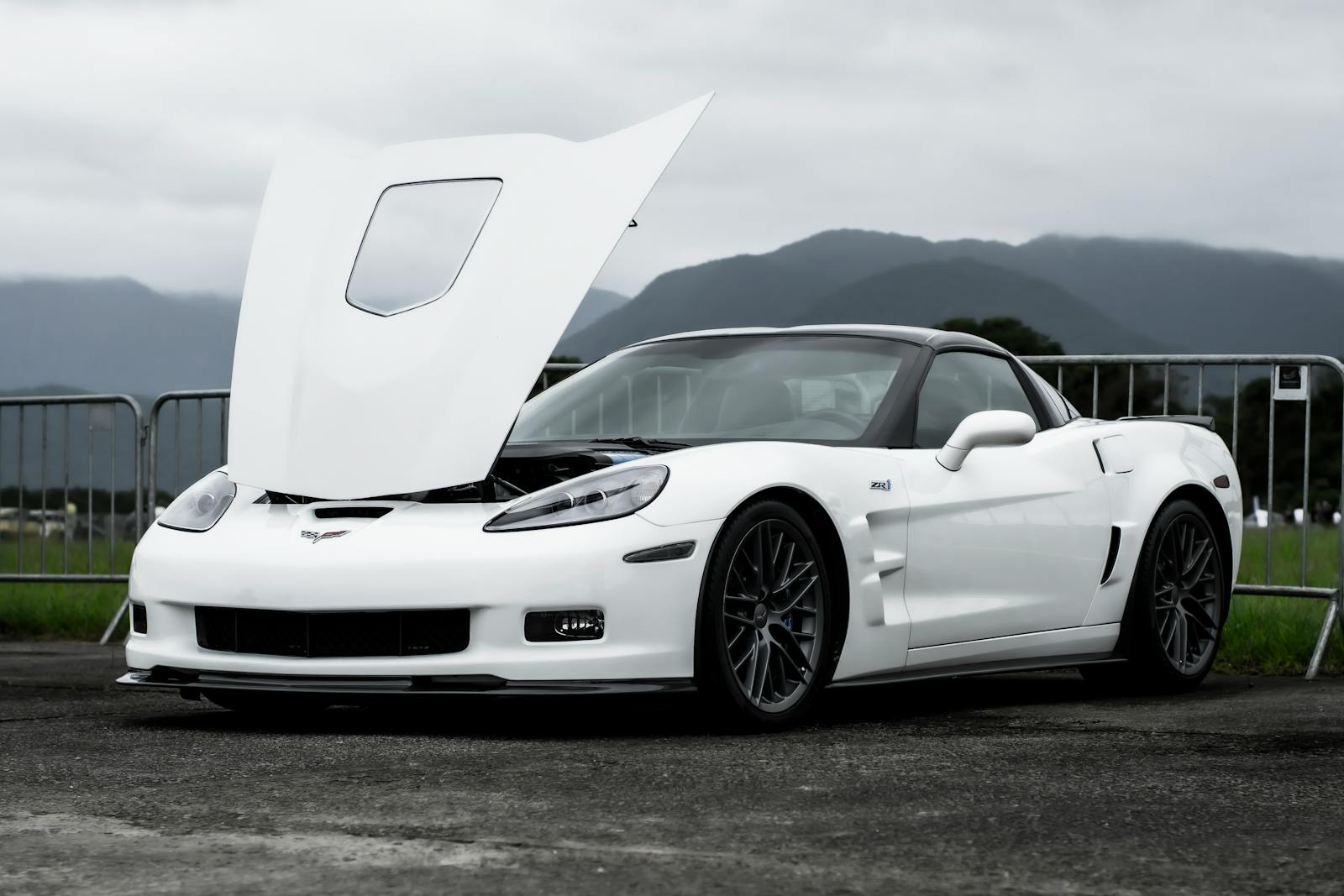 Front view of a white Chevrolet Corvette sports car with open hood against a mountainous backdrop.