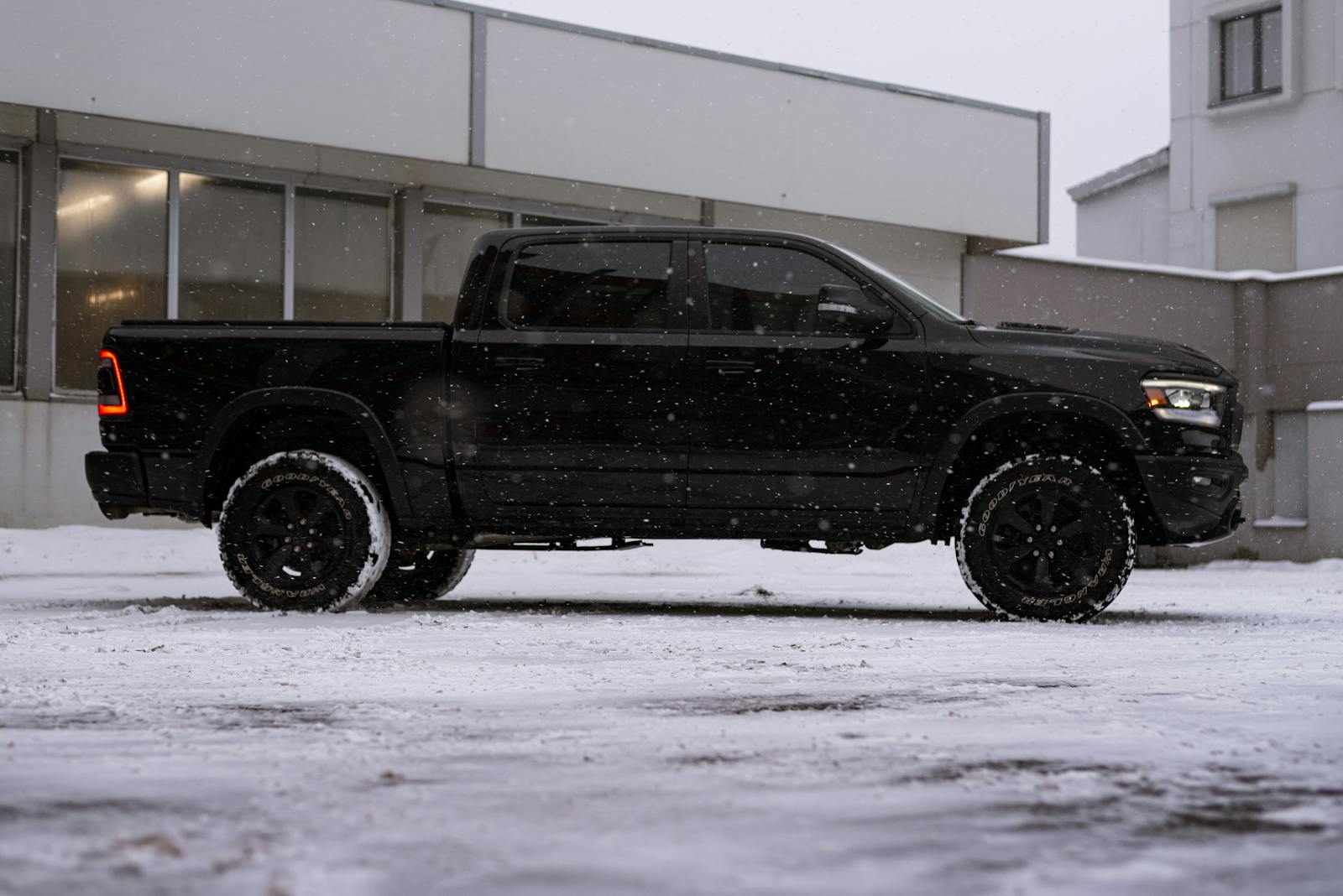Black pickup truck covered in snow parked in a city setting during wintertime.