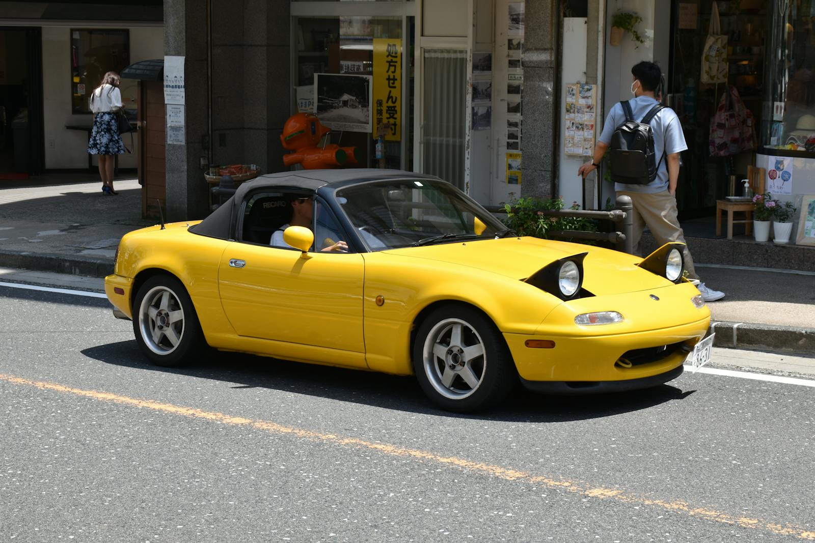 A vibrant yellow sports car driving through a bustling city street on a sunny day.