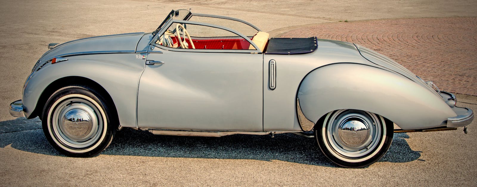 Classic vintage silver convertible car parked outdoors in a sunny location, showcasing elegant design.