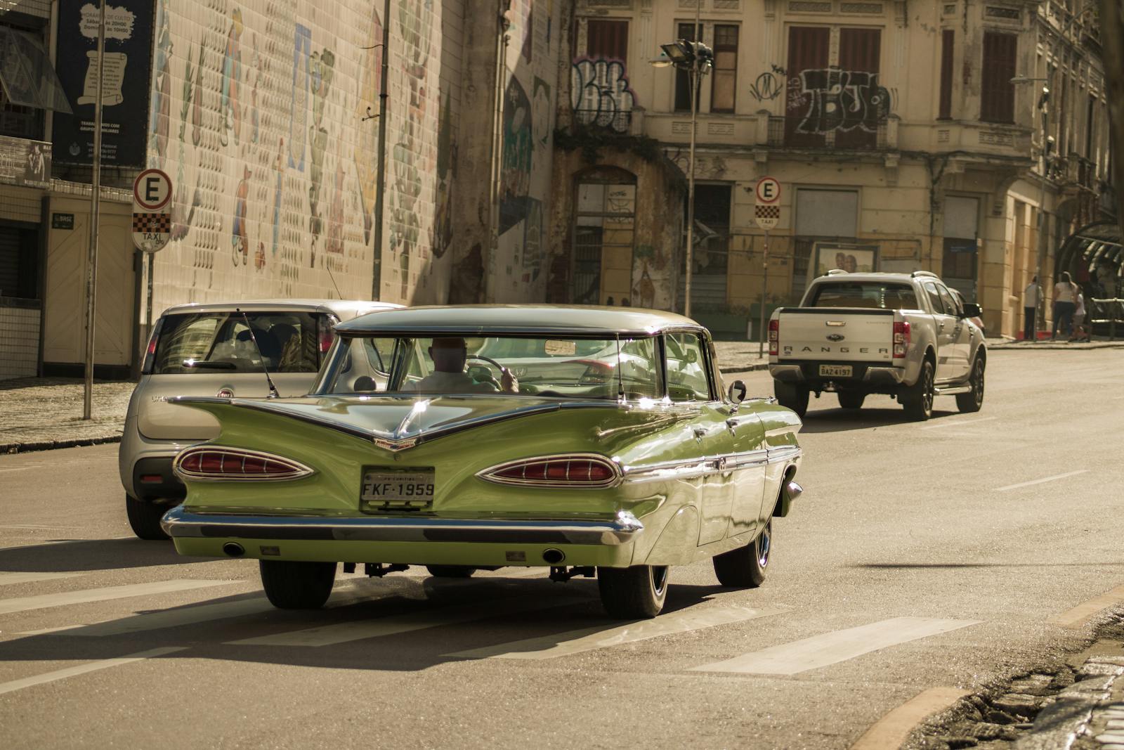 Classic green Chevrolet Impala cruising down a city street lined with historic buildings.