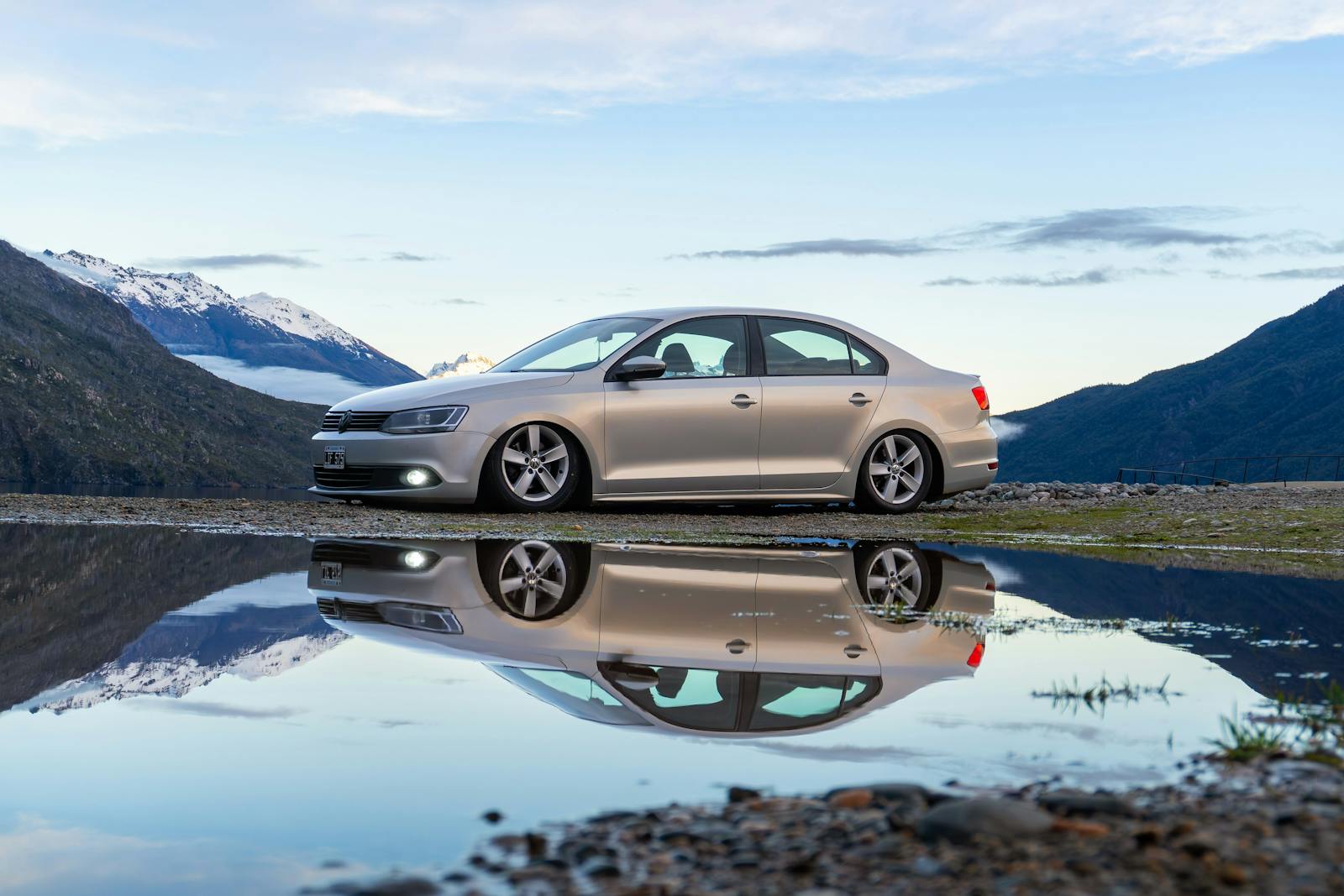 A Volkswagen Jetta parked near Lago Puelo, Chubut, Argentina, reflecting in a puddle with mountain views.