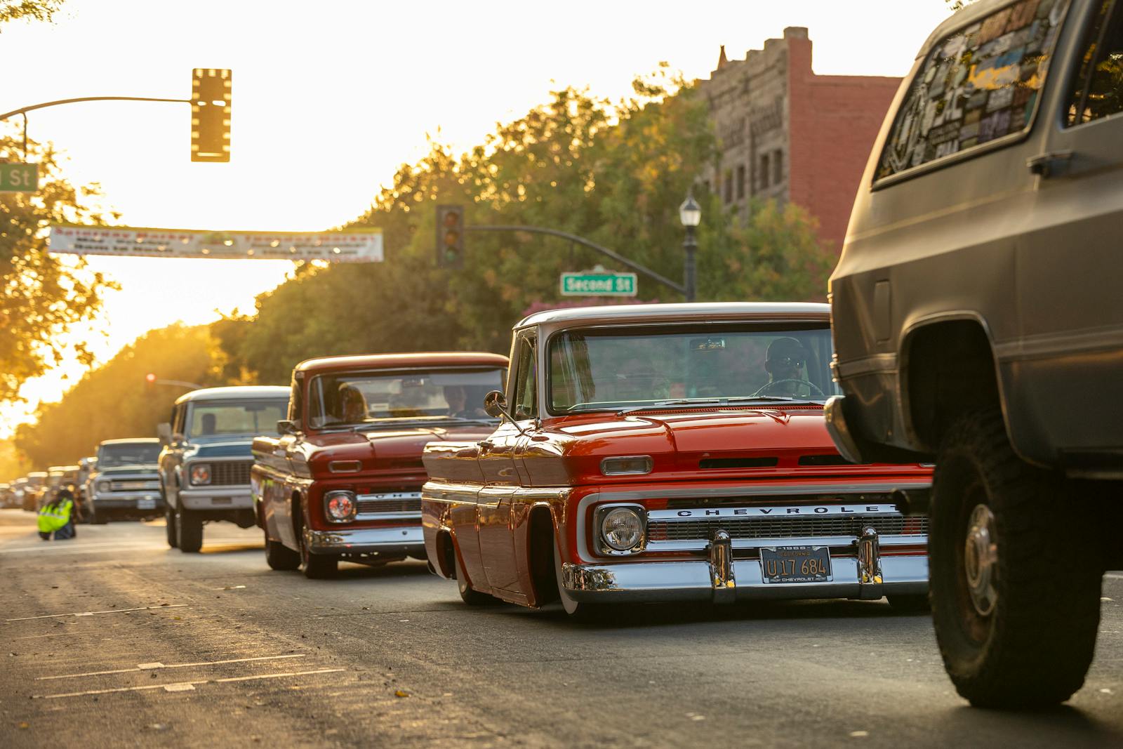 Vintage Chevrolet trucks cruising down a sunlit city street during a retro car show.