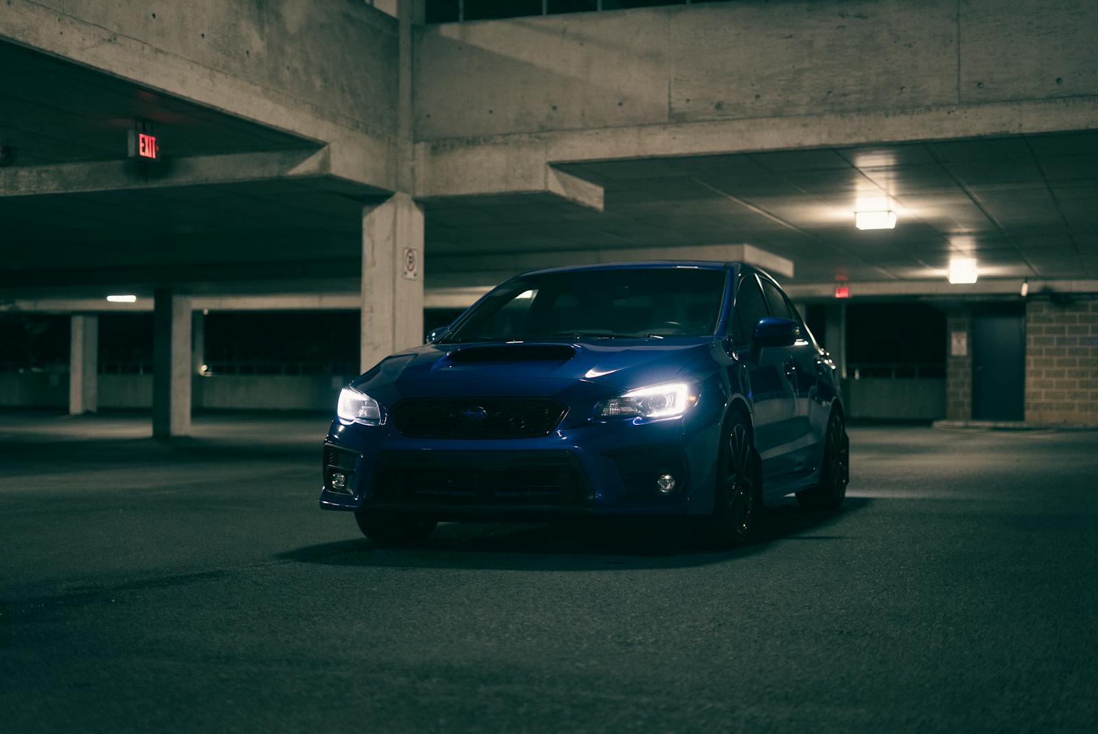 A sleek blue car parked in a dimly lit urban parking garage at night.