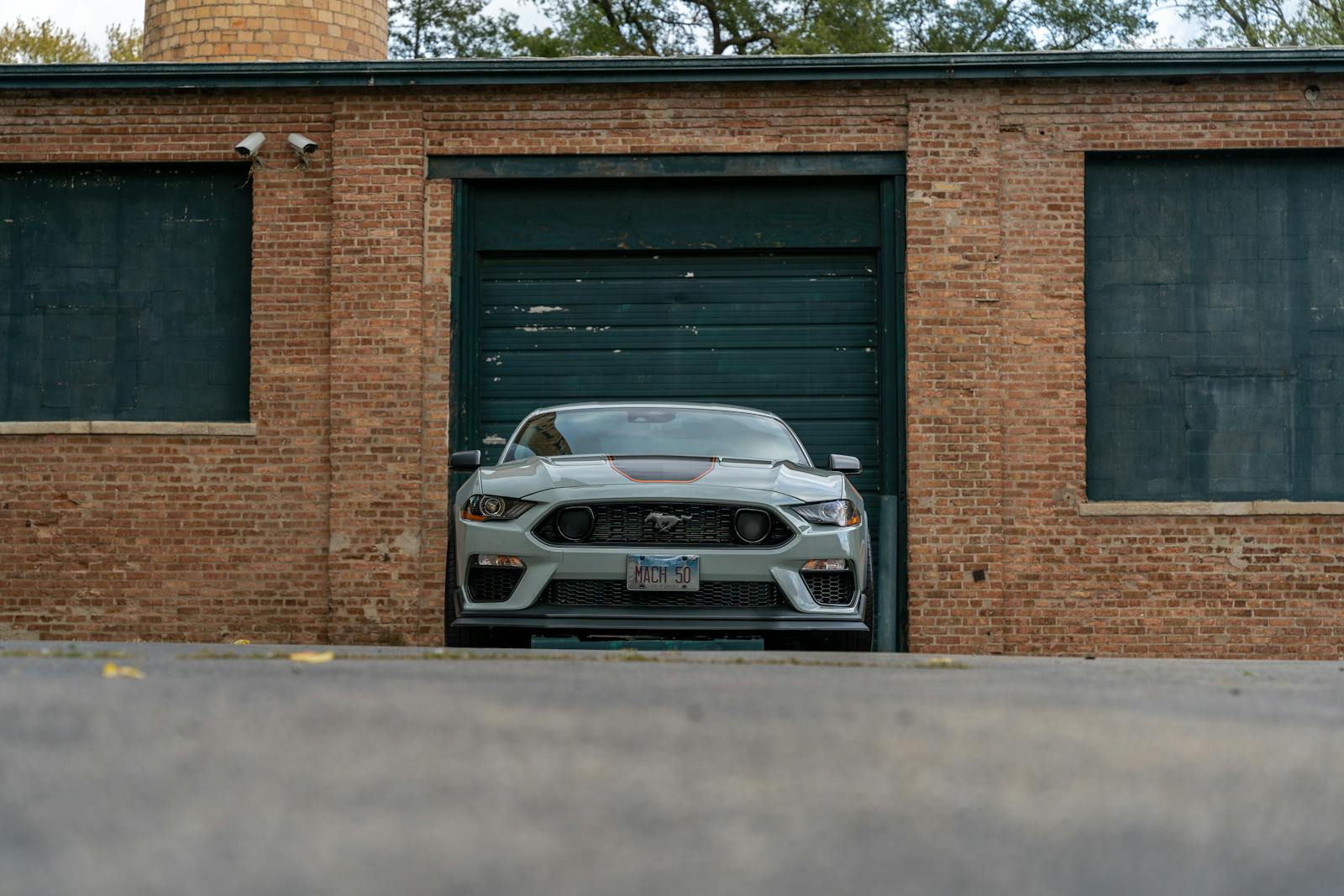 Gray Ford Mustang Mach-E in front of brick building garage door, showcasing sleek design.