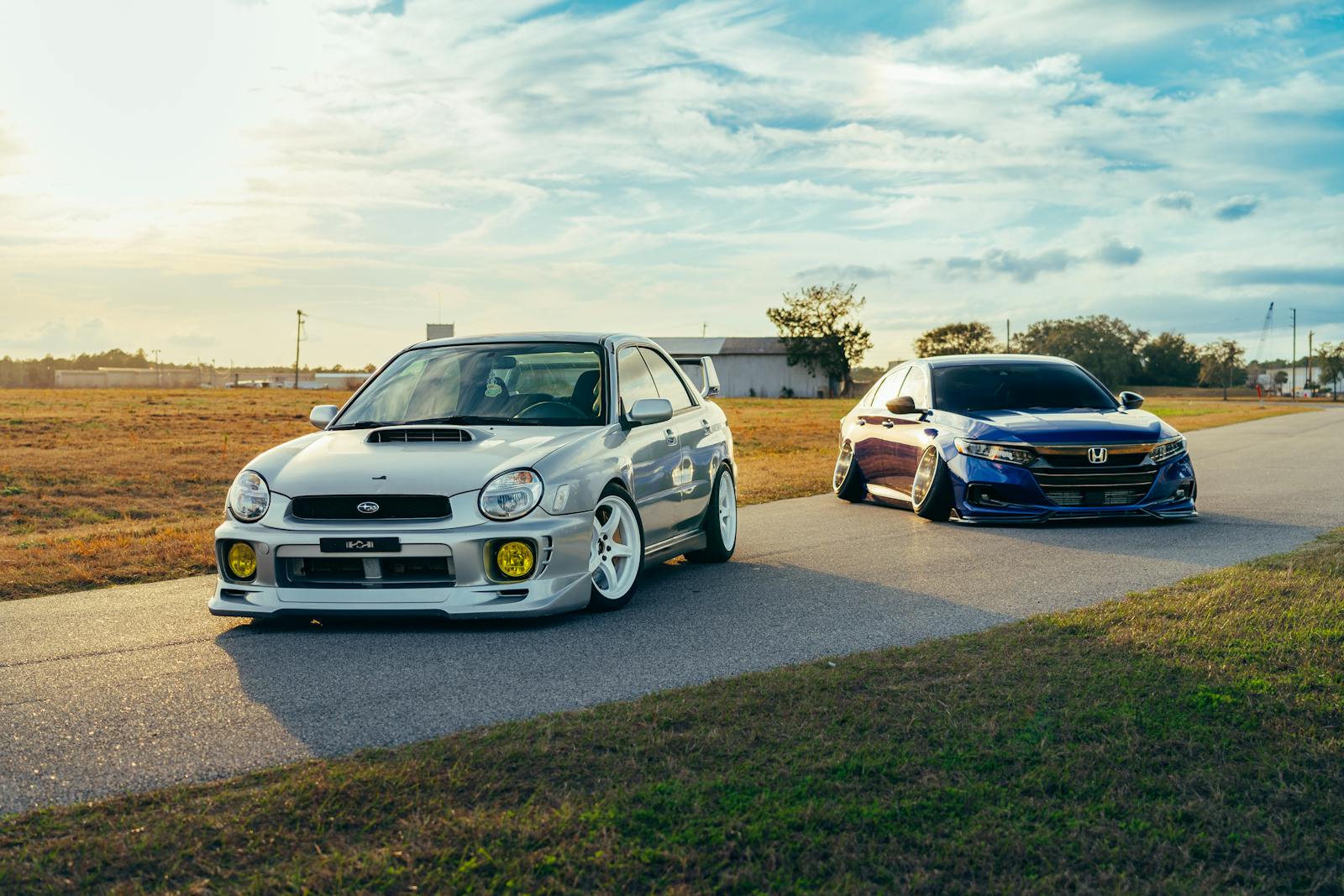 Two modified cars parked on an open road under a blue sky, showcasing automotive style.