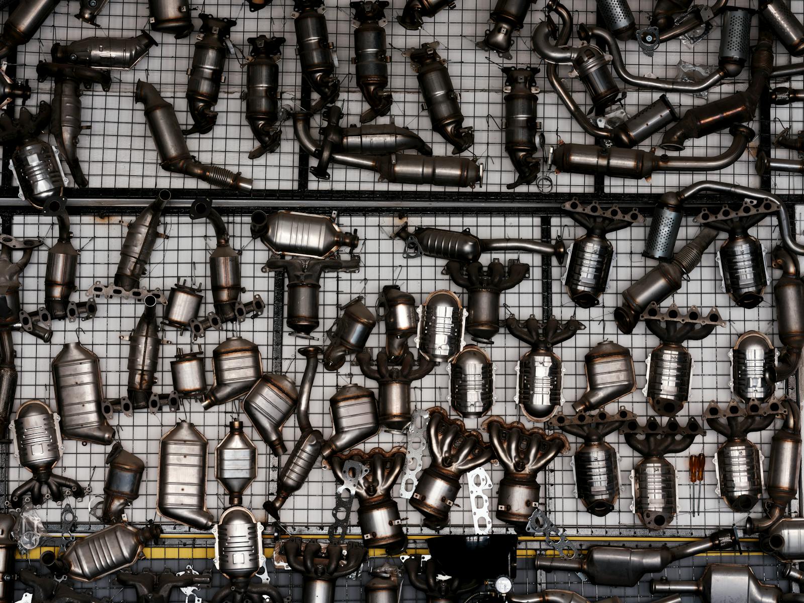 An array of automotive exhaust parts displayed on a grid wall in an industrial garage setting.