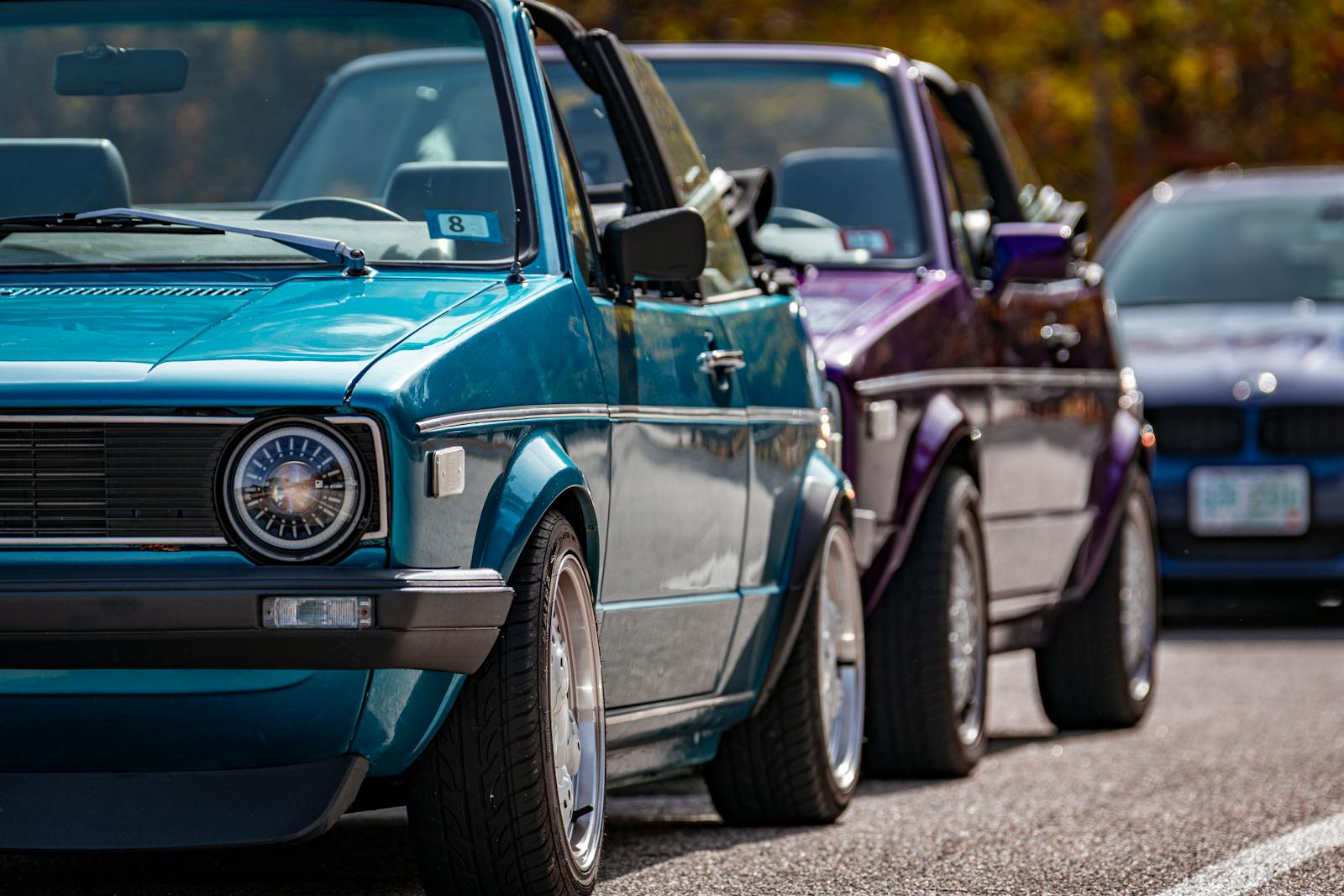 Close-up of vintage convertible cars in bright colors, perfectly aligned in an open parking lot, showcasing classic design.
