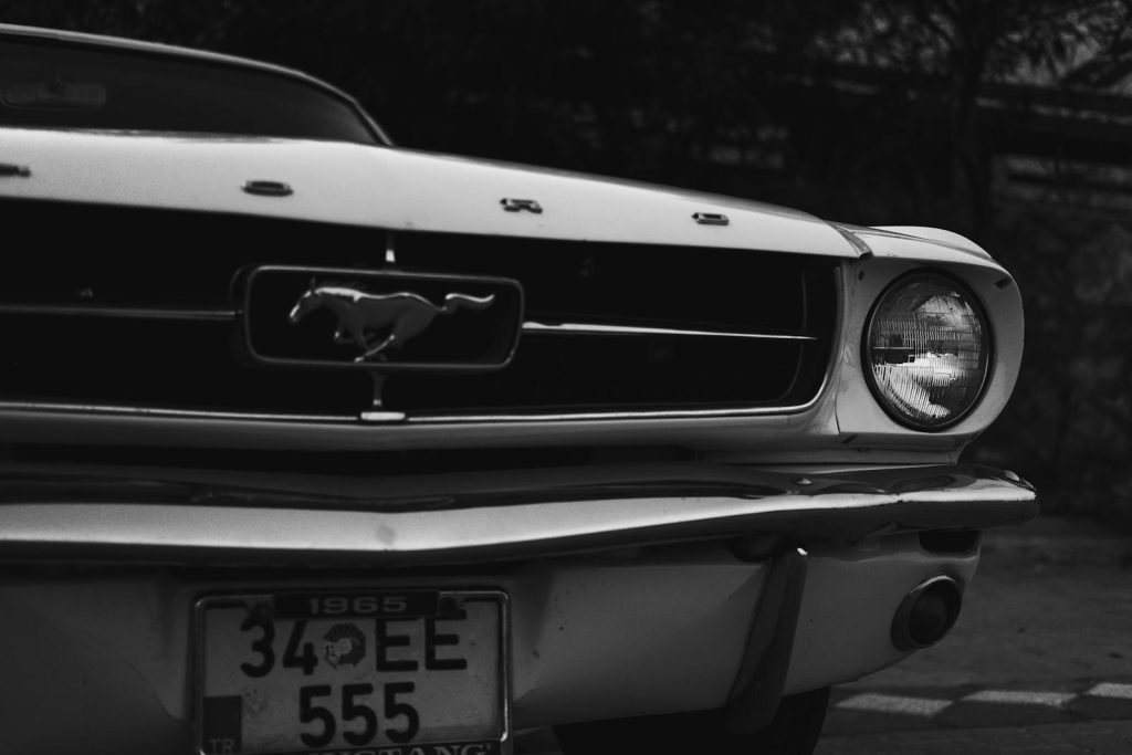 Grayscale image of a classic 1965 Ford Mustang with focus on the car's front grille and emblem.