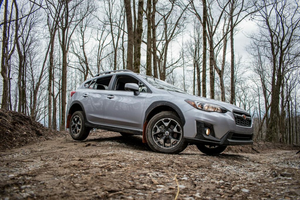 A silver SUV car driving on a rocky dirt road through a forest, showcasing off-road capabilities.