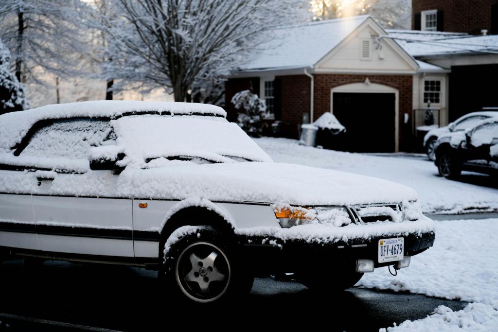 A parked white car covered in snow on a suburban street during winter.