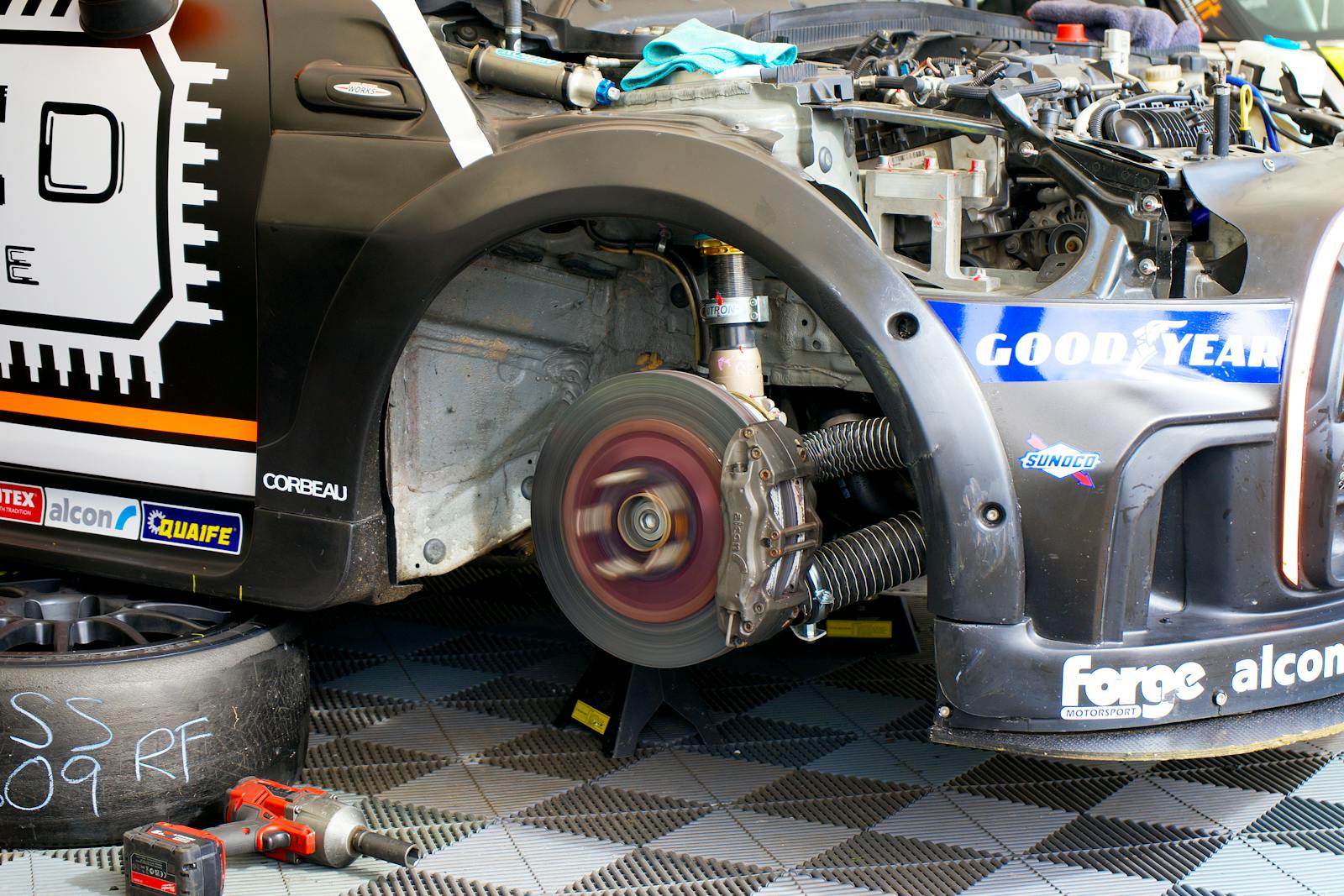 Close-up of race car undergoing maintenance in Silverstone, showing disc brake and tools.