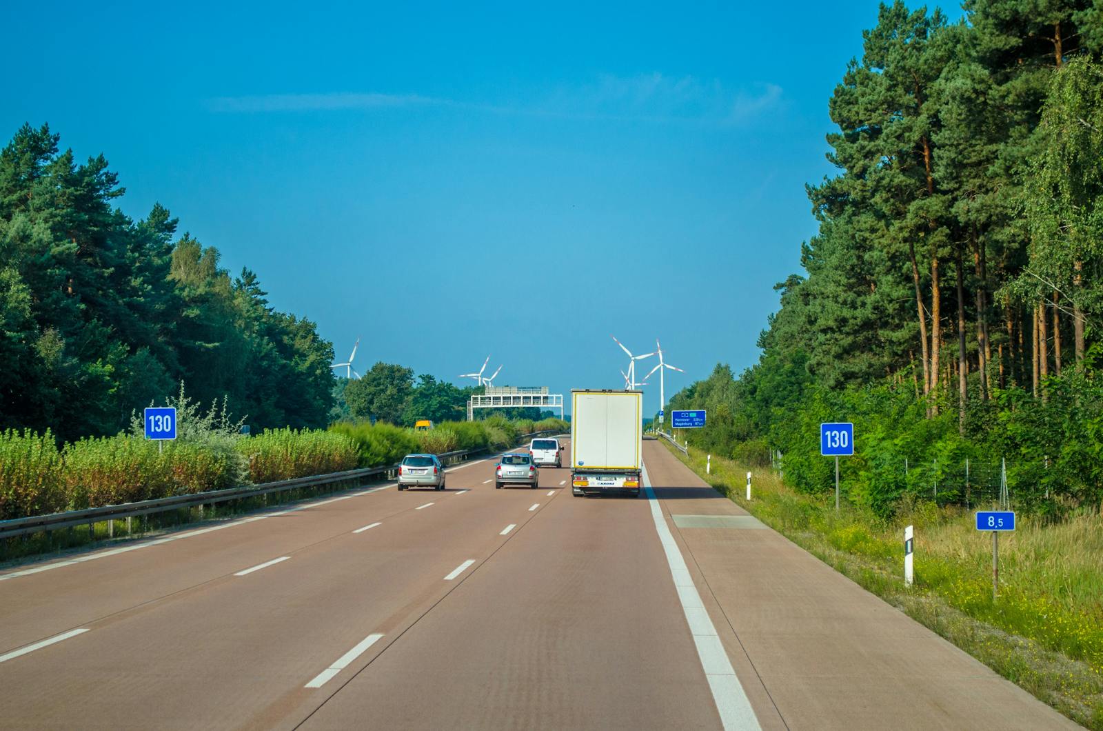 Cars and trucks driving on a highway surrounded by lush greenery and wind turbines.