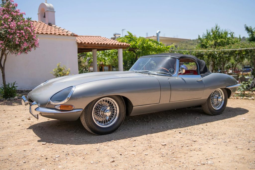 Vintage Jaguar E-Type convertible parked in a sunny yard, showcasing luxury and nostalgia.