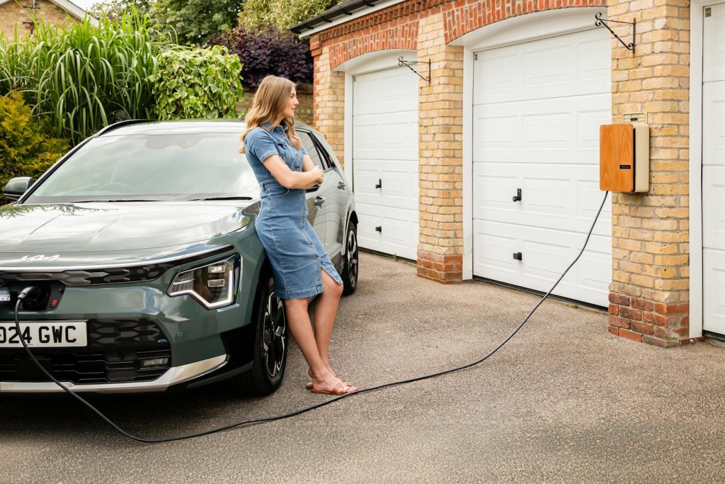 Woman charging electric vehicle at home with a modern wall-mounted charging station.