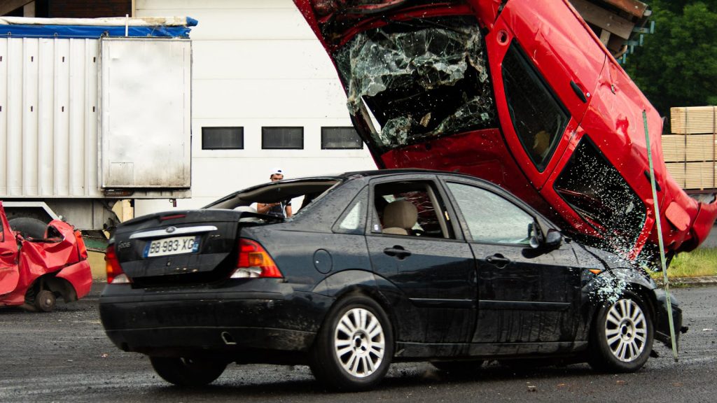A thrilling car stunt crash with a red car flipped onto a black vehicle in an outdoor setting.